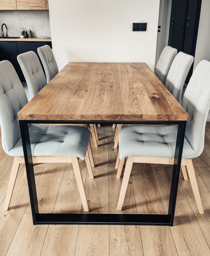 Stół drewniany z blatem z litego drewna dębowego i stalowym stelażem w kształcie ramki, otoczony jasnoszarymi krzesłami w nowoczesnym wnętrzu.